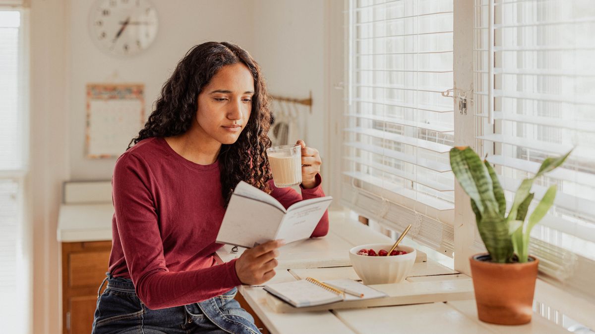 A sister reading the daily text while enjoying her breakfast. A daily planner sits in front of her, and a calendar is on a nearby wall.
