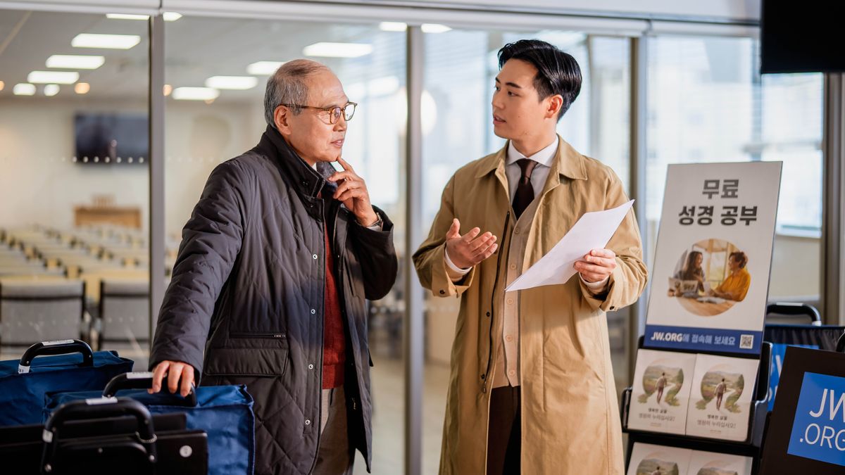 An older elder listening attentively to a young elder explain how to set up a public witnessing cart.