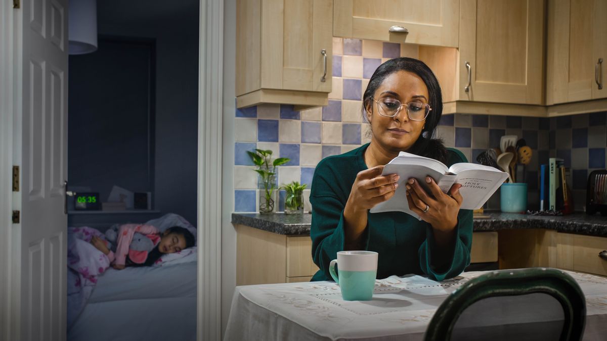 A mother reading the Bible early in the morning while her daughter is still asleep.