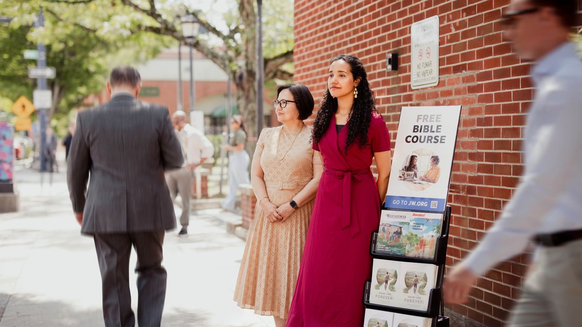 The sister participating in cart witnessing with another sister while people walk by.