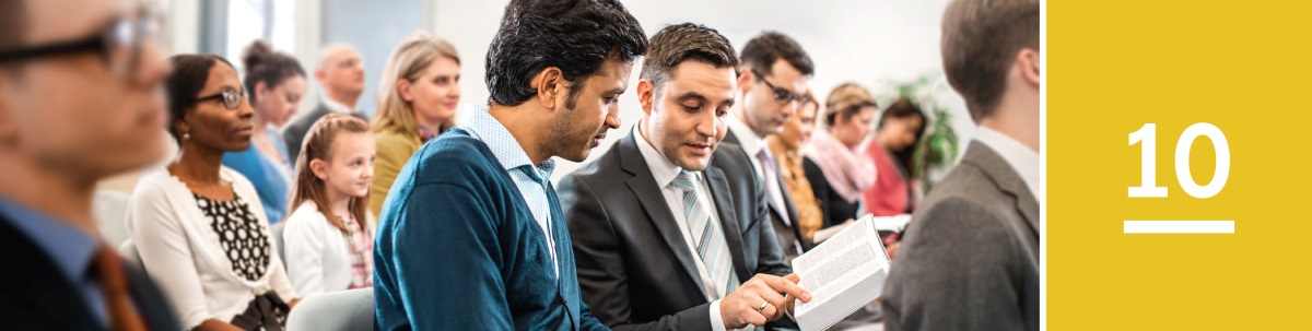 Lesson 10. A man looks at a scripture that a Witness shows him in the Bible during a congregation meeting of Jehovah’s Witnesses.