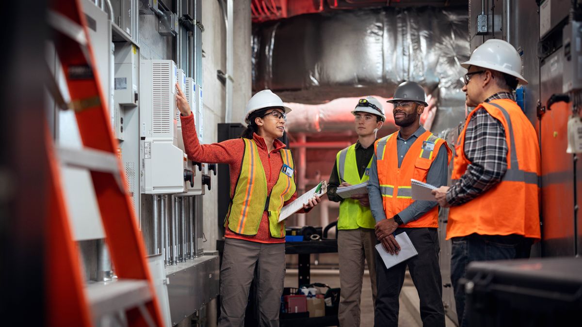 A sister training three brothers how to operate heating and cooling equipment. They listen intently and take notes.