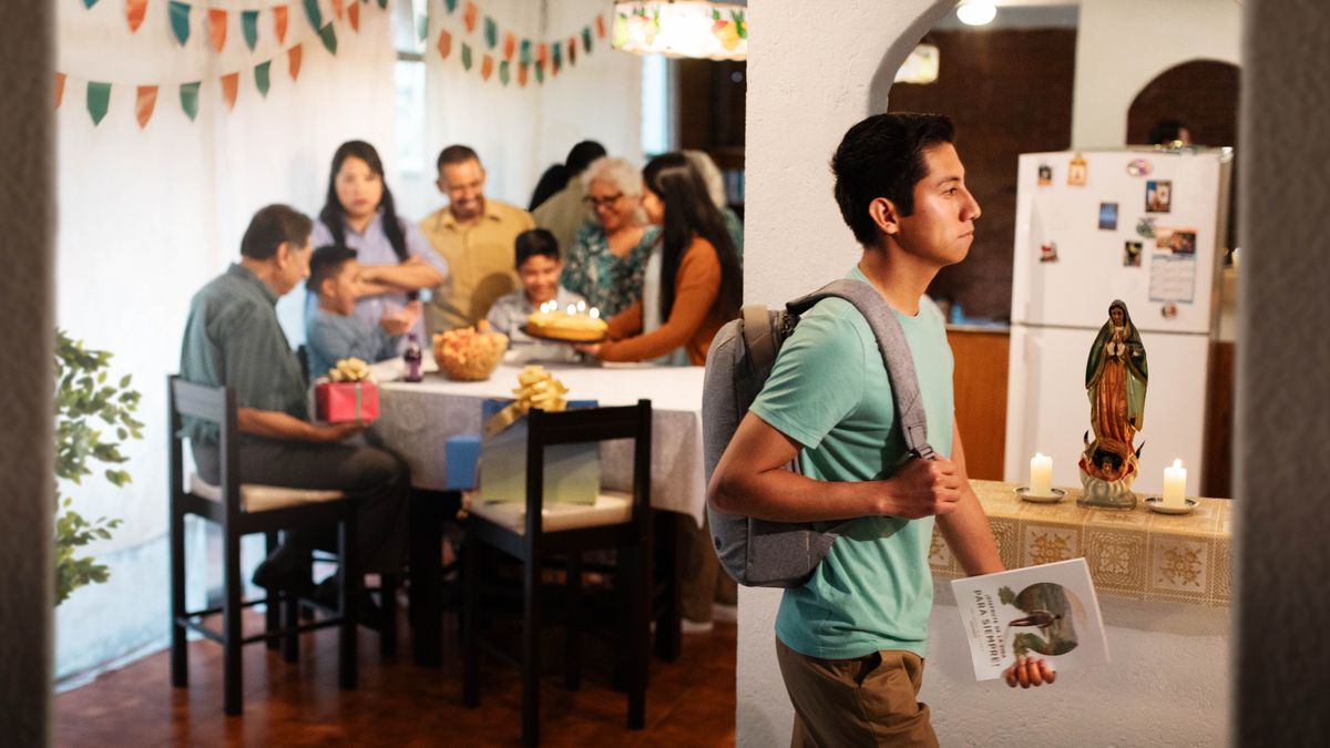 A young man walking confidently away from his family, who are enjoying a birthday celebration. He is holding the “Enjoy Life Forever!” book. One unhappy family member stares at him with her arms crossed.